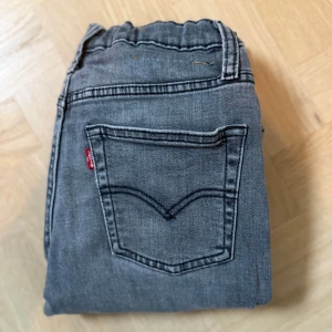 Grå Levi's 501 jeans - Säljer ett par grå Levi's 501 jeans med klassisk femficksdesign och röd Levi's-tag på bakfickan. Jeansen har rak passform och är tillverkade i slitstarkt denimtyg. Perfekta för dig som gillar en tidlös och avslappnad look.