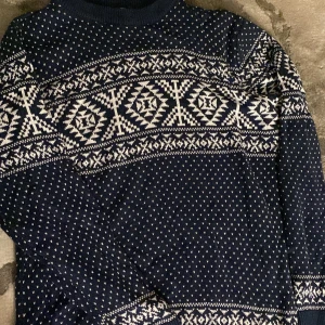 Mörkblå stickad mönstrad tröja - Säljer en mörkblå stickad tröja med vitt nordiskt mönster över bröstet och små vita detaljer över hela tröjan. Perfekt för mysiga och kalla dagar! 