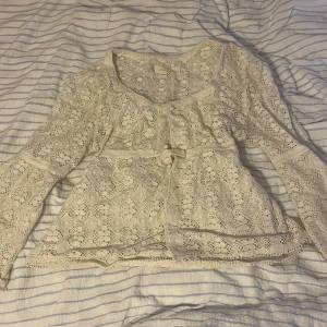 Vit spetsblus från Vous Êtes - Superfin vit spetsblus från Vous Êtes med  ärmar och knytband i midjan. Blusen har vackra spetsdetaljer, rundad halsringning och små knappar framtill. Perfekt för dig som gillar romantisk och bohemisk stil. 