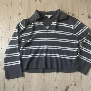 Randig grå tröja från Aware - Grå tröja från Aware med vita horisontella ränder. Tröjan har en krage, v-ringning och långa ärmar. Har även slits på båda sidorna, strl s och bra passform. Sparsamt använt och ser ny ut.