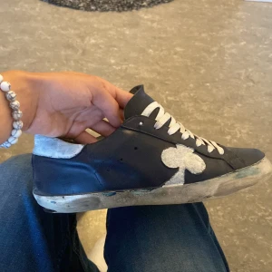 the gallerist skor - Snygga mörkblå sneakers med vit sula och vita skosnören. Skorna har en unik vit klöverdetalj på sidan och ljusgrå häl. Perfekta för dig som gillar en personlig stil och vill sticka ut lite extra. står storlek 40 men passar 41-42