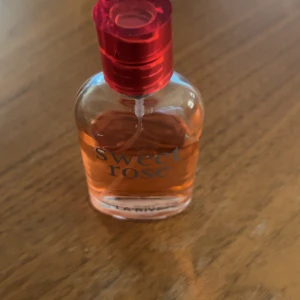 Sweet Rose parfym från La Rive - Söt parfym från La Rive med namnet Sweet Rose. Flaskan är genomskinlig med rosa-orange vätska och har en rundad form. Korken är metallicröd och ger en fräsch känsla. Perfekt för dig som gillar blommiga och fruktiga dofter.