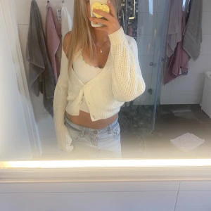 Vit croppad kofta med knappar - Superfin vit stickad kofta med croppad passform och stora knappar framtill. Tröjan har lång ärm och en snygg, avslappnad look som passar perfekt till jeans eller kjol. Enkel att styla och riktigt fräsch till hösten eller sommaren.