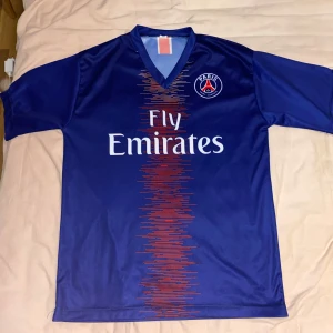 PSG Neymar Jr #10 matchtröja blå - Snygg PSG fotbollströja i blått med röd och vit detalj framtill, Neymar Jr och nummer 10 på ryggen. Paris Saint-Germain klubbmärke på bröstet och Fly Emirates-tryck på framsidan. (Priset kan diskuteras). 