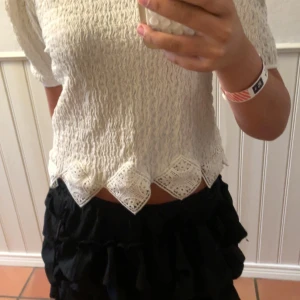 Vit blus med spetskant från Zara - Supersöt vit blus från Zara med kort puffärm och unik spetskant nertill i geometriskt mönster. Tyget är lätt strukturerat och blusen har en lite croppad passform. Perfekt för dig som gillar romantiska detaljer och vill sticka ut lite extra. Använd ca 2-3 gånger men kommer som ny