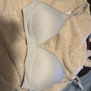 Beige bandeau från Lindex - Säljer en enkel och stilren beige bandeau från Lindex. Toppen har justerbara axelband och mjuka kupor för extra komfort. Perfekt under toppar eller klänningar där du vill ha en diskret look. Materialet är mjukt och stretchigt för en skön passform.