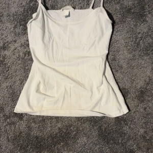 Vit linnetopp med smala axelband - Enkel och stilren vit linnetopp med smala axelband. Perfekt att matcha med jeans eller kjol för en clean look. Mjuk och skön känsla, passar till alla tillfällen när du vill ha något basic men snyggt.
