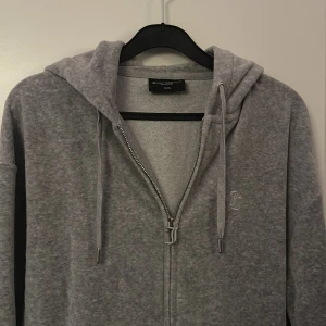 Ljusgrå zip up hoodie från Juicy Couture XXS - Mjuk grå oversized hoodie från Juicy Couture med dragkedja, huva och snörning. Broderad JC-logga på bröstet och kängurufickor framtill. Perfekt för chill dagar och enkel att matcha med andra plagg.