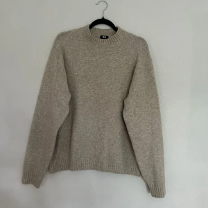 Beige stickad tröja från Uniqlo - Mysig beige stickad tröja från Uniqlo i storlek M. Tröjan har en klassisk rund halsringning, ribbade muddar och är långärmad. Perfekt för lager-på-lager och chill höst- eller vinterstil.
