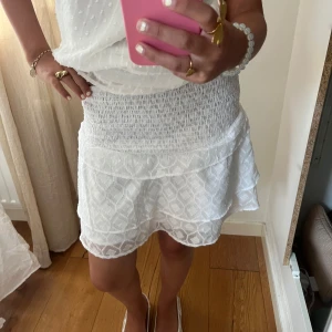 Vit kort kjol med volang och smock - Supersöt vit kort kjol med bred smock i midjan och volangkant. säljer den för att den inte kommer till användning 