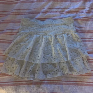 Vit spetskjol med volanger från H&M - Supersöt vit kortkjol från H&M med två lager volanger och blommig spets. Kjolen har bred midja och är perfekt för dig som gillar romantisk och feminin stil. Passar till både sneakers och sandaler.