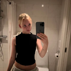 Svart ärmlös linnetopp - Säljer en svart, enkel och stilren ärmlös linnetopp med hög hals. Toppen är figurnära och har en clean look utan synliga detaljer eller mönster. Perfekt att matcha med jeans eller kjol för en snygg och avslappnad stil.