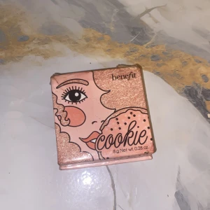Benefit Cookie highlighter - Supersnygg highlighter från Benefit i nyansen Cookie. Kommer i en söt rosa ask med spegel i locket. Ger en intensiv, champagnefärgad glow med skimrande finish. Perfekt för att framhäva kindben, näsrygg och amorbåge.