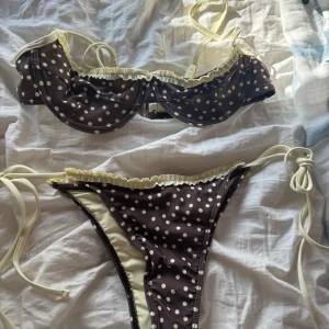Brun prickig bikini med volangdetalj - Superfin bikini i brun med krämvita/ljusgula prickar och krämvita/ljusgula volangdetaljer. Överdelen har bygel och smala axelband, underdelen har höga skärningar och knyt i sidorna. Perfekt för strandhäng och poolparty!