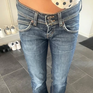 Lågmidjade bootcut jeans från Lee - Säljer ett par snygga blå jeans från Lee med låg midja och bootcut-ben. Jeansen har slitna detaljer, dubbla knappar i midjan och klassiska fickor fram och bak. Storlek W27 L31, skriv för frågor och prisförslag! Kan gå ner i pris mycket!💗