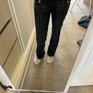 Bootcut jeans från H&M, mörkblå, stl 152 - Mörkblå bootcut jeans från H&M med låg midja och justerbar midja. Klassisk femficksmodell med snygga kontrastsömmar och diskret tvätt. Perfekta för dig som gillar en avslappnad men ändå trendig look.