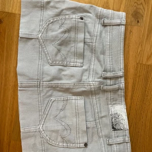 Ljusgrå jeanskjol med fickor - Snygg ljusgrå jeanskjol med coola detaljer som  fickor både fram och bak, bälteshällor och silvrig patch. Kjolen har dragkedjor på fickorna framtill och markerade sömmar som ger en streetig vibe.