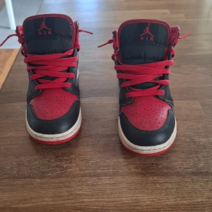 Nike Air Jordan 1 Mid Svart/Röd EUR 38 - Säljer ett par Nike Air Jordan 1 Mid i klassisk svart och röd färg. Skorna har snörning, perforerad tå och vit sula. Ovandelen är i skinn och textil, med ikonisk Jumpman-logga på plösen. Perfekta för dig som gillar streetstyle och sneakers med attityd. Priset går att diskutera.