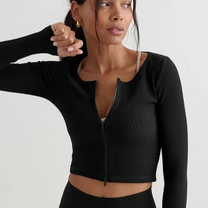 Svart ribbad kofta från Aim'n - Säljer en svart ribbad kofta från Aim'n med dragkedja framtill. Tröjan har långärmad design och är tillverkad i ett stretchigt syntetmaterial som sitter snyggt på kroppen. Perfekt att slänga över en topp för en chill look.