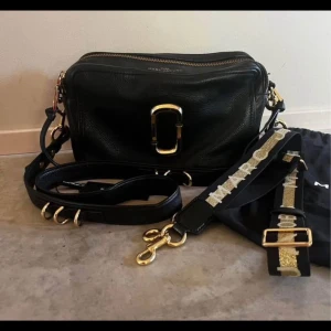Svart axelväska från Marc Jacobs - Äkta Marc Jacobs-väska av modellen The 27  med dustbag och extra axelrem av modellen Bag Strap Slim Logo. Se bilder och googla för mått :)   Väskan är rymligare än Snapshot och i fint skick. Detta är en perfekt handväska till hösten 2025! Väldigt stilren och rare🍀  Nypris totalt: 6498:-  Säljes för 3000:-    PRUTBAR VID SNABB AFFÄR! ✅