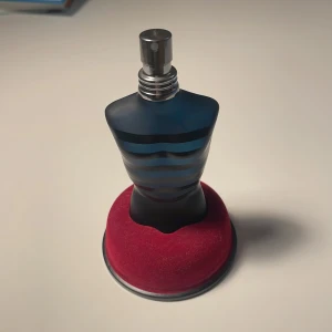 Jean Paul Gaultier Ultra Male parfym - Säljer en Jean Paul Gaultier Ultra Male parfym i den ikoniska flaskan formad som en manlig torso. Flaskan är matt mörkblå med svarta ränder och har en metallisk spraytopp. Kommer med original svart cylinderförpackning med röd text.