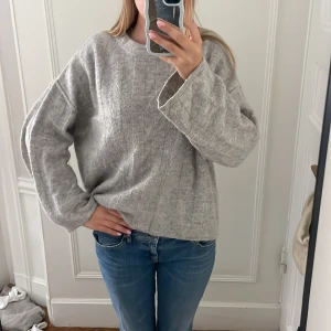Grå loose stickad tröja - Säljer en chill grå stickad tröja med loose passform och långa ärmar. Tröjan har en enkel rund hals och ett diskret rutigt mönster i stickningen. Perfekt att slänga på sig när det är lite kyligt ute. Passar dig som gillar en avslappnad stil.