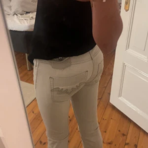  ljusa bootcut jeans - Säljer ett par ljusa jeans med bootcut passform och snygga broderade detaljer på bakfickorna. Byxorna har låg midja