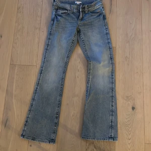 Bootcut jeans från Gina Tricot, blå - Bootcut jeans från Gina Tricot i ljusblå tvätt med klassiska fem fickor och cool knappdetalj på bakfickan. Jeansen har normal passform och är tillverkade i jeansmaterial med snygga slitningar. Perfekt för dig som gillar retrovibbar och bredare ben.