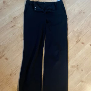 Svarta kostymbyxor från Vero Moda - Snygga svarta kostymbyxor från Vero Moda i storlek M/32. Byxorna har raka ben och klassisk passform med knapp och dragkedja framtill. Perfekta för en clean och stilren look, passar dig som gillar enkel och tidlös stil.