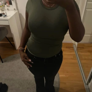 Olivgrön tight kortärmad topp - Säljer en olivgrön topp med korta ärmar. Modellen är figurnära och har en clean, enkel look som är lätt att matcha med jeans eller kjol. Materialet känns mjukt och stretchigt