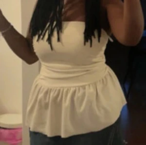 Vit bandeau tubtopp med volang - Säljer en vit bandeau tubtopp med volangkant nedtill. Toppen är axelbandslös och har en snygg, figurnära passform upptill som går ut i en luftig volang. Perfekt för dig som gillar en clean och chic look. Materialet känns mjukt och lätt mot huden.