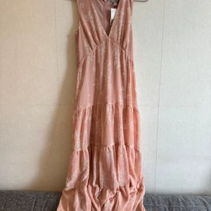 Ljusrosa långklänning med blommigt mönster - Superfin långklänning från H&M i ljusrosa med vitt blommigt mönster. Storlek 32 men som motsvarar 34!!