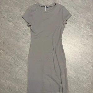 Grå ribbad kortklänning H&M Divided - Säljer en enkel och stilren grå ribbad kortklänning från H&M Divided. Klänningen har rund hals, korta ärmar och är figurnära i modellen. Materialet är mjuk bomull med lite stretch för skön passform. Perfekt att matcha med sneakers eller boots.