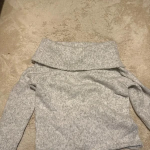 Ljusgrå stickad off shoulder  - Mysig ljusgrå stickad off shoulder. Tröjan har lång ärm och är tillverkad i mjukt stickat material, perfekt för kyliga dagar. Enkel och stilren design som är lätt att matcha med jeans eller kjol.