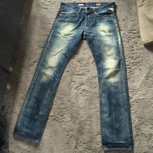 Replay Anbass blå jeans med slitningar - Säljer ett par Replay Anbass jeans i blå tvätt med coola slitningar och blekta detaljer på låren och knäna. Klassisk femficksmodell med Replay-logga på bakfickan och patch bak i midjan. Jeansen har rak passform och snygga kontrastsömmar.riktig snygga jeans men passar inte mig längre, de passar dig som är runt 187-88 lång. Nypris runt 1300kr