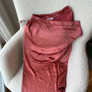 Rosa midikjol från Kappahl - Säljer en elegant långkjol i en mjuk rosa ton från Kappahl. Kjolen har en slät, glansig yta och är tillverkad i ett satinliknande material. 