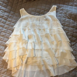 Vit volangblus från H&M Divided - Säljer en vit blus från H&M Divided i storlek 40. Blusen har flera lager med volanger som ger en riktigt flowy och cool look. Den är ärmlös och har rund halsringning. Perfekt för dig som gillar romantiska vibes och vill sticka ut lite extra.