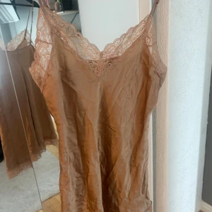 Champagnefärgad nattlinne med smala axelband - Säljer ett nattlinne ifrån intimnisimi som tyvärr har fått en liten rosa fläck längst fram syns på bild 3. Annars väldigt bra skick
