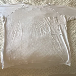 Vit långärmad t-shirt från Risk - Vit långärmad t-shirt från Risk, med rund hals och en enkel bröstficka på vänster sida. Modellen är loose fit och tillverkad i mjuk bomull som känns skön mot huden. 