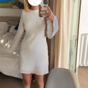 Vit kortklänning med strukturmönster - Superfin vit kortklänning med långärmade ärmar och snyggt strukturmönster i tyget. Klänningen har en rak passform och är tillverkad i ett lätt, luftigt material som känns perfekt för varmare dagar.