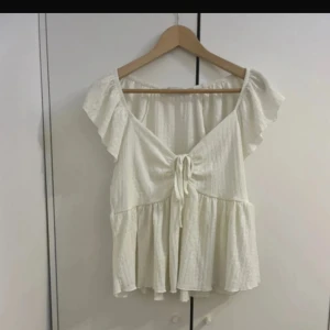 Vit blus med volang från 157 - Supersöt vit blus från 157 med volangärmar och knyt framtill. Blusen har en v-ringad design. 