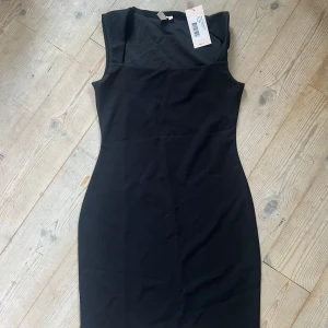 Svart kort klänning från Nelly - Snygg svart klänning från Nelly i kort modell med figurnära passform. Klänningen har ärmlös design och stilren, enkel look som är lätt att matcha med accessoarer. Perfekt för dig som gillar minimalistisk stil och vill ha en klassisk liten svart klänning.