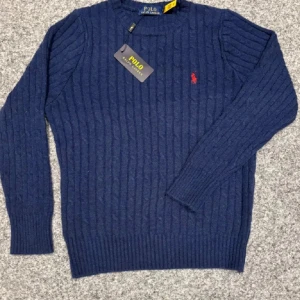 Marinblå stickad tröja Polo Ralph Lauren - Snygg marinblå stickad tröja från Polo Ralph Lauren med klassisk kabelstickning och röd broderad logga på bröstet. Rund hals och långa ärmar, perfekt för dig som gillar stilrena och tidlösa plagg. Passar dig som vill ha en chill men ändå uppklädd look. Tveka inte på att höra av dig, är också intresserad av byten!