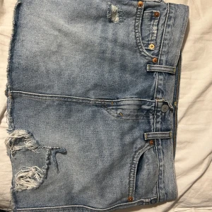 Levi's ljusblå jeanskjol med slits - Säljer en ljusblå jeanskjol från Levi's med rå kant och fransar längst ner. Kjolen har en cool slits framtill och klassiska fickor både fram och bak. Perfekt för dig som gillar avslappnad och trendig denimstil. 