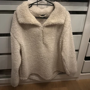 Vit fleece-tröja från Gina Tricot - Supermysig vit fleece-tröja från Gina Tricot med halv dragkedja och stor krage. Tröjan har långärmade ärmar och är tillverkad i fluffigt syntetmaterial som ger en cool teddy-look. Perfekt för kalla dagar när du vill vara både varm och snygg. Passar även S om du vill ha den oversized.