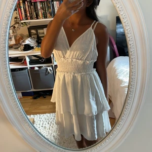 Vit omlottklänning från SHEIN - Supersöt vit kortklänning från SHEIN i storlek S. Klänningen har omlottskärning med v-ringad front, smockad midja och dubbla tunna axelband som korsas i ryggen. Kjolen är volangig och materialet är lätt polyester, perfekt för varma dagar.