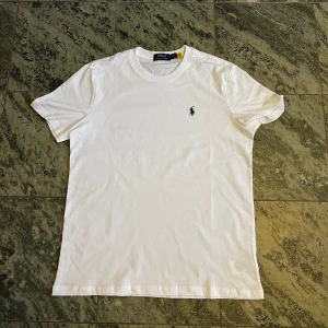 Vit t-shirt från Polo Ralph Lauren - Klassisk vit t-shirt från Polo Ralph Lauren med liten broderad logga på bröstet. T-shirten har rund halsringning och är tillverkad i mjuk bomull. Perfekt för en stilren och enkel look. Nyskick.