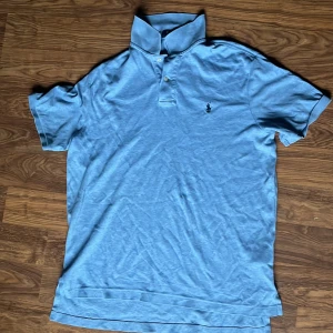 Ljusblå Polo Ralph Lauren t-shirt - Snygg ljusblå t-shirt från Polo Ralph Lauren med klassisk krage och korta ärmar. T-shirten har broderad logga på bröstet och knappar vid halsen. Tillverkad i mjuk bomull som är skön mot huden. Perfekt för dig som gillar stilren och enkel design.