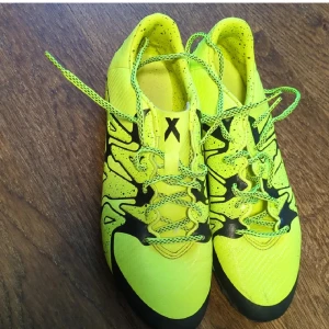 Professionella fotballskor - Snygga profesionalla fotbollsskor från Adidas i neon-gult med svarta detaljer och coolt grafiskt mönster. Skorna har snörning och en yttersula med fasta dobbar för bra grepp på planen. Tillverkade i syntetmaterial.