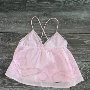 Ljusrosa broderad linnetopp Gina Tricot - Supersöt ljusrosa linnetopp från Gina Tricot med tunna korsade axelband och broderade detaljer framtill. Toppen har spetskant vid bysten och är lätt och luftig i bomull, perfekt för varma dagar. Passar dig som gillar romantisk och feminin stil.